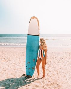 a woman holding a surfboard on top of a sandy beach