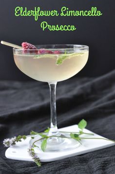 a glass filled with liquid and garnished with raspberries sitting on a white plate