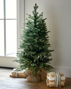 a small christmas tree with presents under it on the floor next to an open window