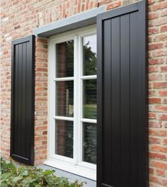 an open window with black shutters on a brick building