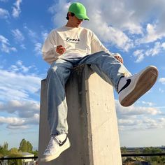 a young man sitting on top of a cement block while looking at his cell phone