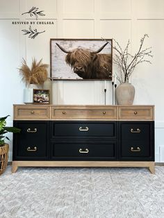 a black dresser with two drawers and a painting on the wall above it in a living room