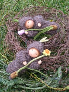 three little stuffed animals sitting in a nest on the ground with flowers growing out of it