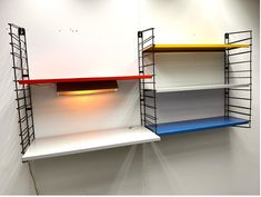 three shelves with different colors on them in a white walled room, one has a lamp and the other is empty