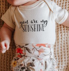 Show the little one in your life the joy they bring you with this screen printed "You Are My Sunshine" infant onsie. Featuring 100% combed ring-spun cotton with built-in stretch for easy movement. The three-snap bottom closure design makes for quick & easy changing. Cotton Letter Print Bodysuit As Gift, Baby Shirt Ideas, Simple Onesie Designs, Cotton Bodysuit With Letter Print As Gift, Cotton Bodysuit With Letter Print For Playtime, Baby Girl Cricut Onesies, Cute Cotton Onesie With Custom Print, Personalized Cotton Onesie For Playtime, Baby Onsies Ideas