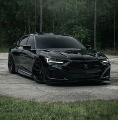 a black acura is parked in front of some trees