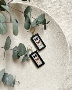 two framed pictures hang from the side of a white wall next to some green leaves