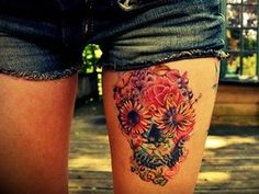 a woman's thigh with sunflowers and skulls tattoo on her leg, in front of a house