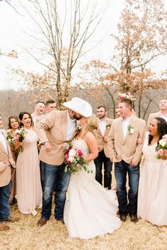 a bride and groom kissing in front of a group of people wearing cowboy hats on their wedding day