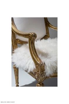 an ornate chair with white fur on the back and gold trim around the armrests