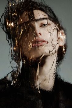 a woman's face is covered in gold foil and water droplets as she stares into the distance