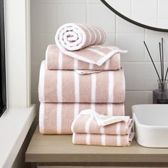 towels stacked on top of each other in front of a mirror and bowl with toothbrushes next to it