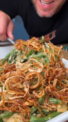 a bowl filled with green beans and onion rings next to a man eating something out of it