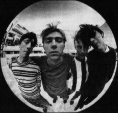 three young men are standing in front of a circular mirror with one man's face partially obscured by the other