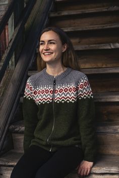 a woman sitting on the steps wearing a sweater and smiling at the camera with her hands in her pockets