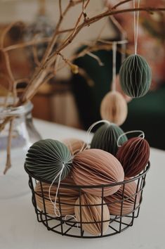 some balls of yarn are in a wire basket on a table with paper lanterns hanging from the branches