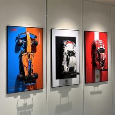 three framed photographs of cars on display in a room with white walls and flooring