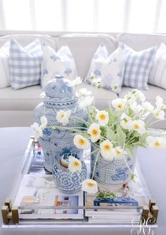 blue and white vases with flowers on a tray in front of the couches