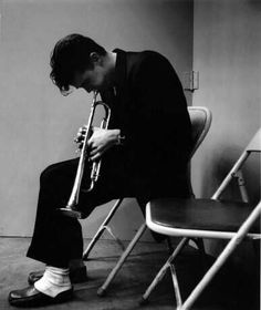 black and white photograph of a man playing a trumpet in a room with chairs around him