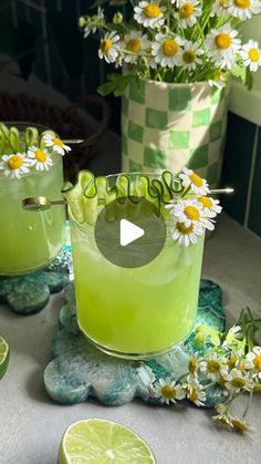 two glasses filled with limeade and daisies on a table next to flowers in vases