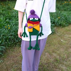 a person standing in the grass wearing a purple hat and green scarf with a frog on it