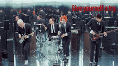 three men in suits and ties are playing guitars while another man with red hair stands behind them