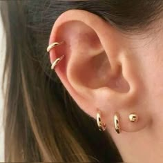 a woman's ear with three small gold hoops