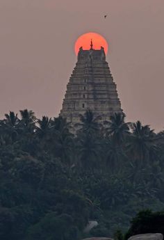 the sun is setting in front of a temple on top of a hill with palm trees