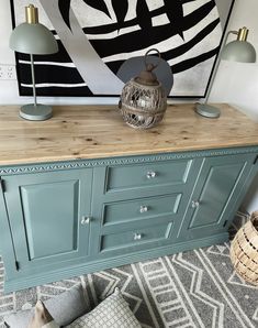 a blue dresser with two lamps on top and a painting above it in the background