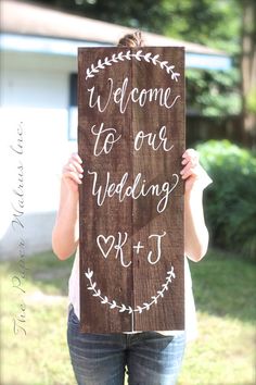 a woman holding up a wooden sign that says welcome to our wedding ktj