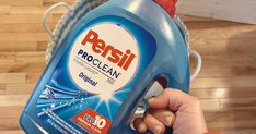 a hand holding a bottle of persil proclean on top of a wooden floor