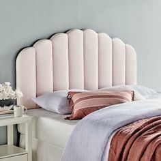 a pink headboard on top of a bed next to a night stand and nightstand