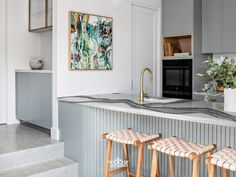 two stools sit in front of a kitchen counter with an art piece on the wall