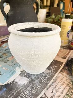 a large white vase sitting on top of a table next to a black and white pot