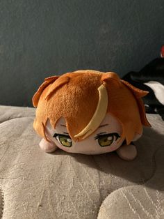 an orange stuffed animal with horns on it's head sitting on a bed next to a pillow