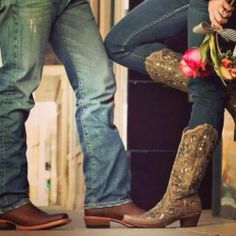 two people standing next to each other with boots and flowers in their lap, one holding onto the leg of another person's boot