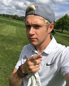 a man in a hat and white shirt holding his hand out while standing on a golf course