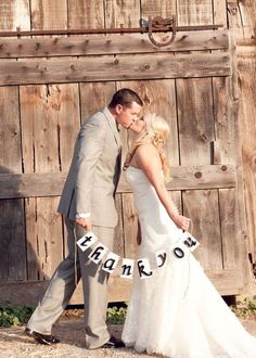 a bride and groom kissing in front of a wooden fence with the word thank you on it