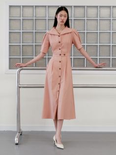 a woman standing in front of a metal rail wearing a pink dress and white shoes