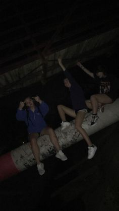 three people sitting on top of a fire hydrant at night with their arms in the air