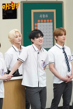 group of young men standing next to each other in front of a desk with writing on it