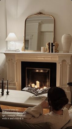 a woman sitting on a couch in front of a fire place with candles and a mirror