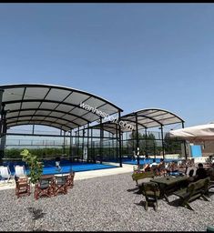 an outdoor swimming pool with tables and umbrellas next to it, under a blue sky