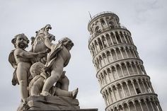 the leaning tower has statues on it and is next to a statue of an angel