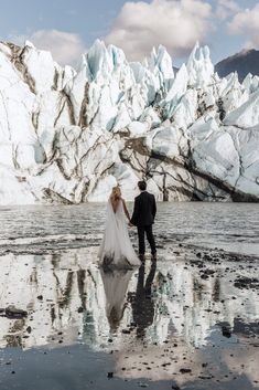 a bride and groom holding hands walking on the beach in front of icebergs