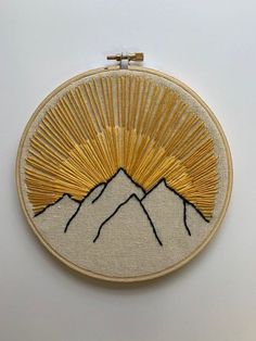 a hand embroidered wall hanging with mountains in the background and gold thread work on it