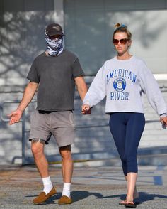 a man and woman walking down the street holding hands with one another while wearing bandana's