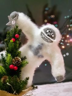 a white stuffed animal sitting on top of a christmas tree next to a pine cone