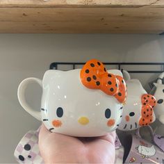 a hello kitty coffee mug with an orange bow on it's head and polka dots