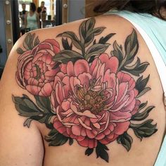 a woman's back with flowers on it and leaves around her shoulder, as well as an arm tattoo